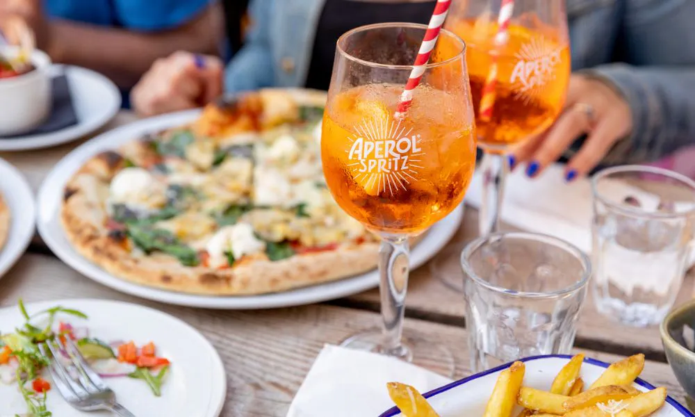 a selection of pizzas and aperol spritzes on a table