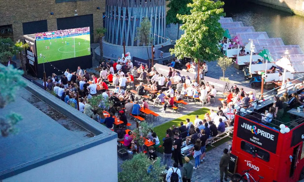 fans watching football on giant screen with red bus behind