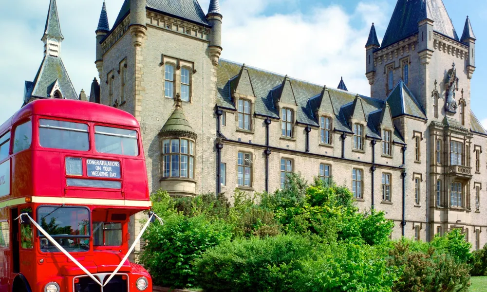 large castle building with red double decker wedding bus