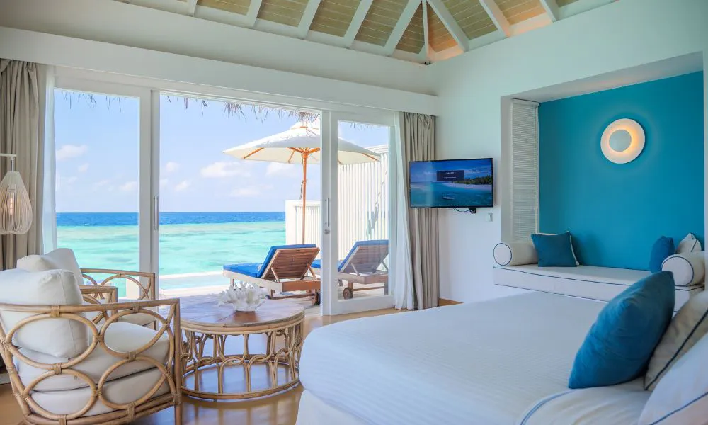 The bedroom in a water villa, with blue cushions on a white bed