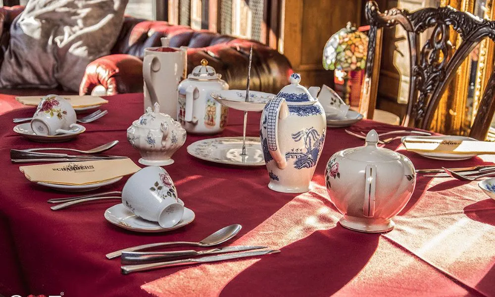 a table set for afternoon tea with teacups and teapots 