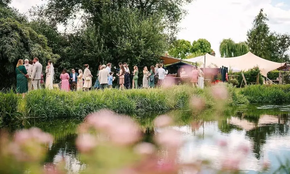 wedding guests gathering in a garden with a river and a marquee