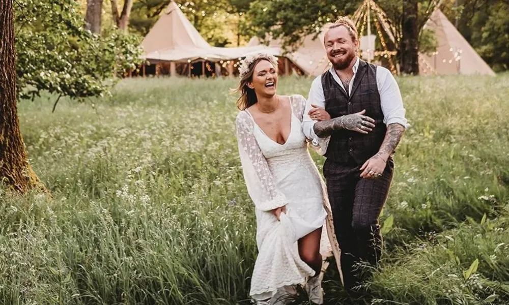 Bride and groom with woodland tipi reception behind