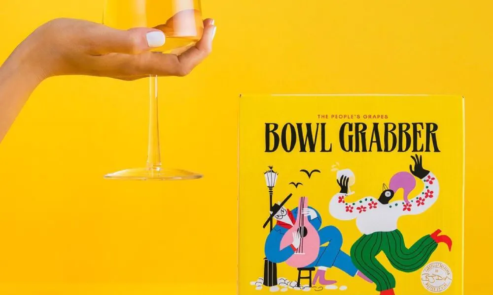 yellow background with someone holding a wine glass and boxed wine