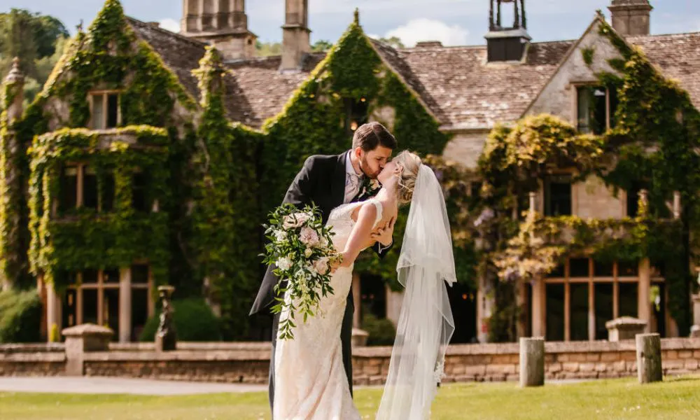 bride and groom kiss in front of old manor house