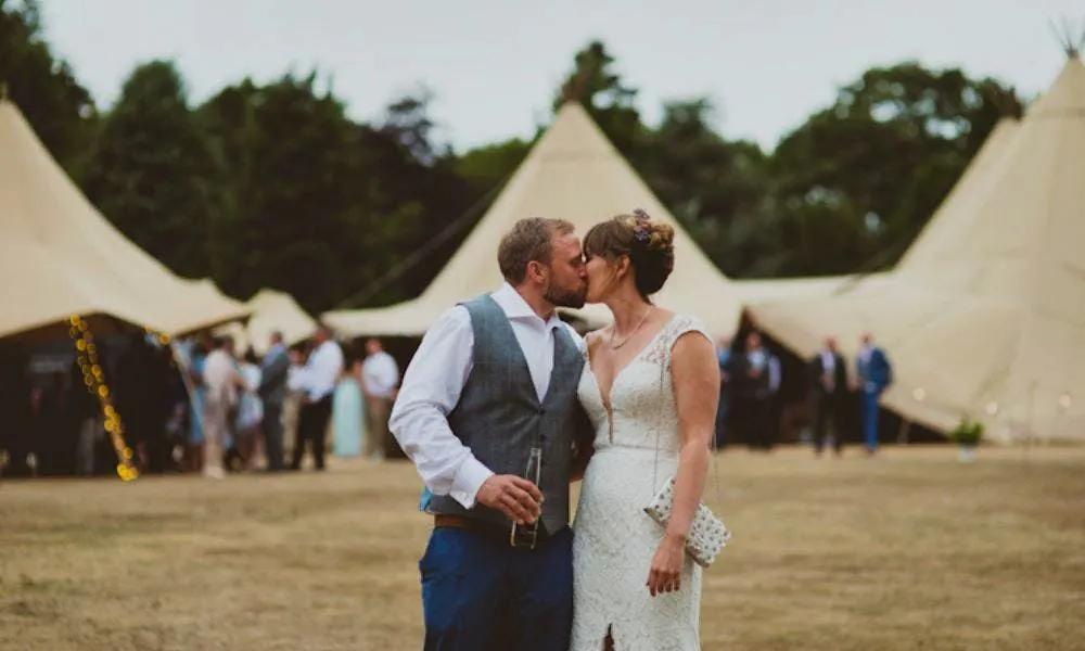 couple kiss with tipi wedding in the background