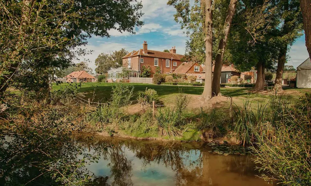 red brick house by a river surrounded with trees