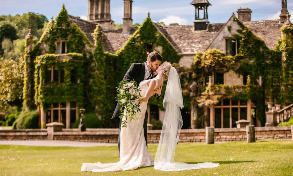 bride and groom kiss outside large old manor house
