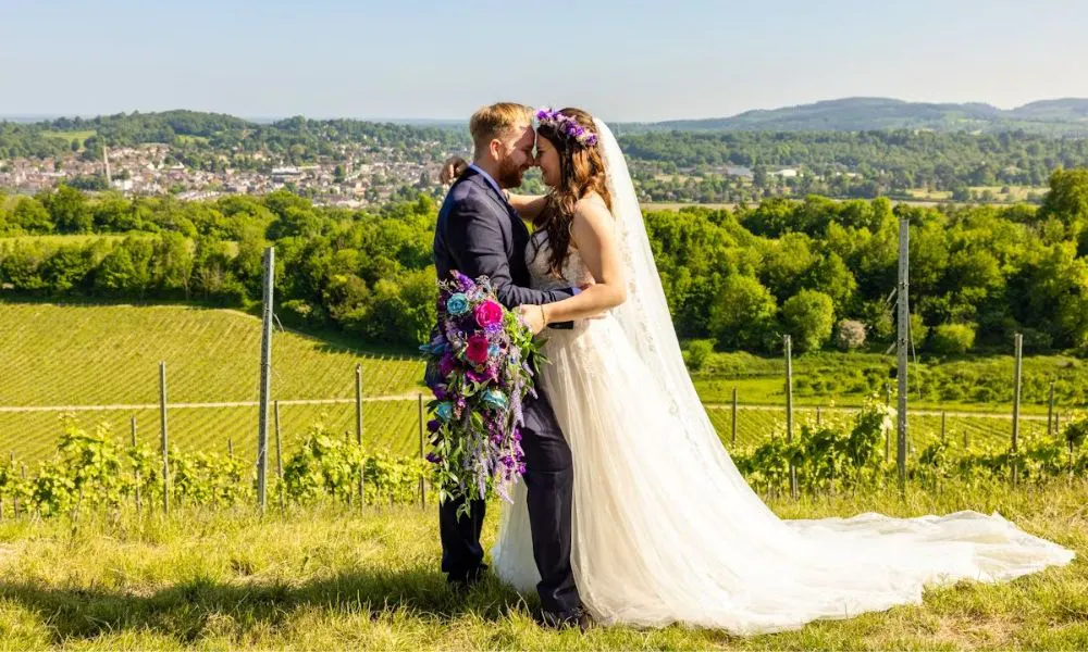 A bride holding a colourful summer bouquet in front of a vineyard wedding venue