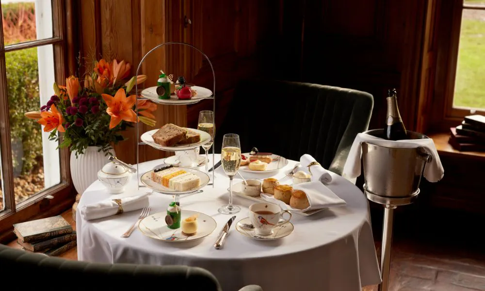 a white-clothed table set with afternoon tea, and served with a bottle of Champagne