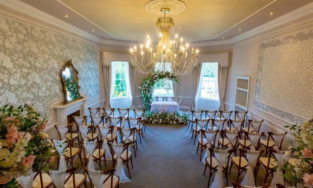 a wedding reception setup in a grand room with bay windows and a chandelier