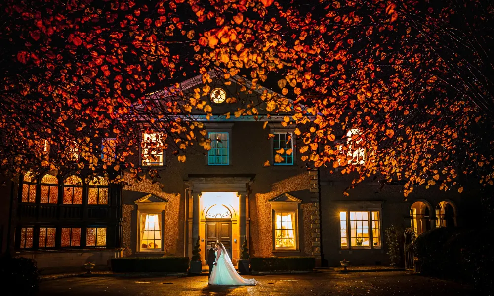 wedding couple in front of house framed by autumn leaves