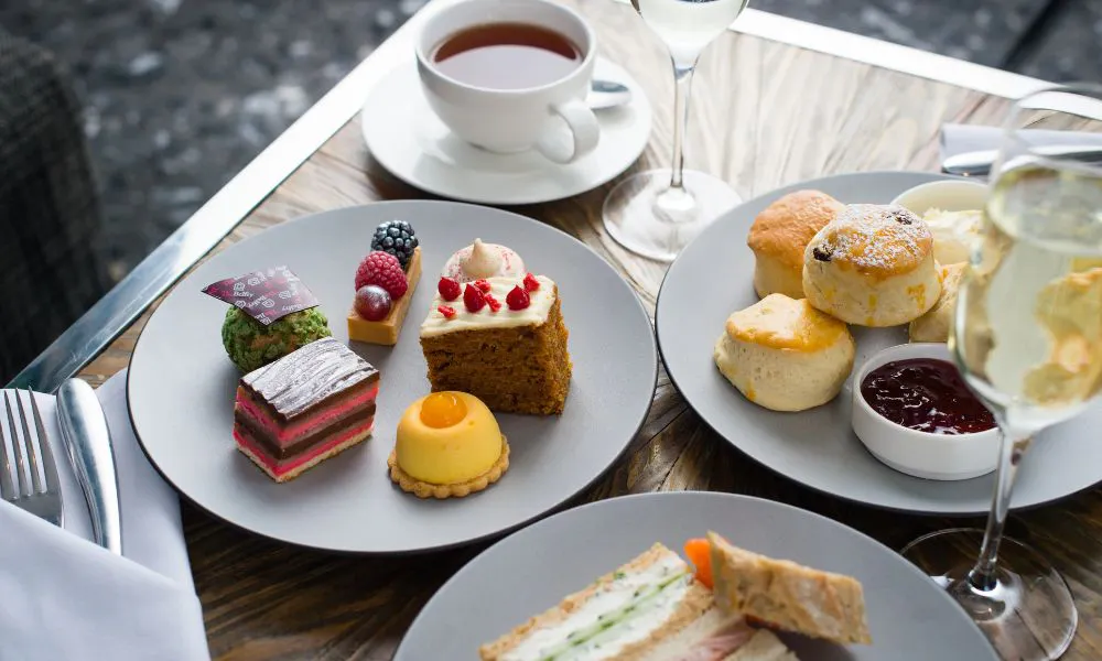 a table set with plates of scones, sandiwhces and pastries