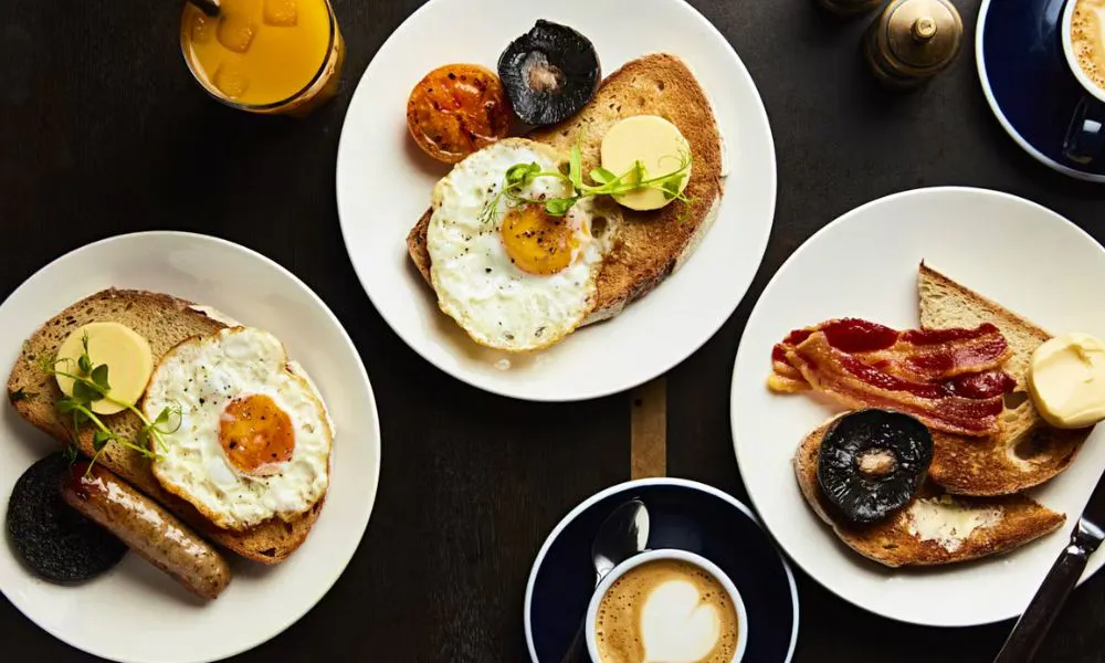 Brunch spread with fried eggs, bacon and sausages on toast, with a couple of coffees