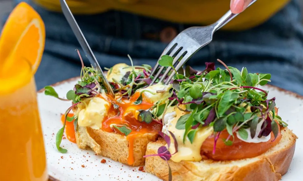 Someone cutting into eggs royale, with a glass of orange juice