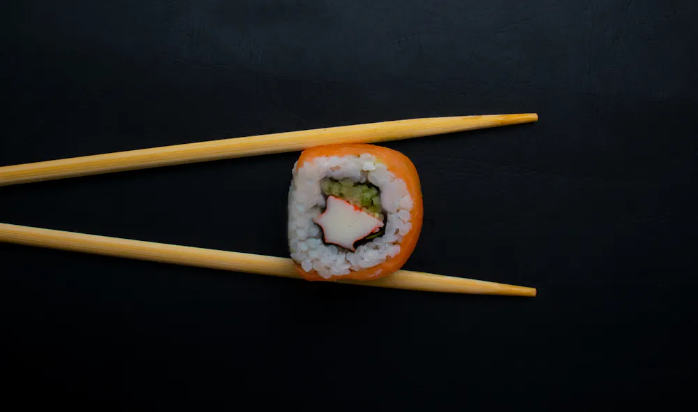 A piece of sushi in between chopsticks
