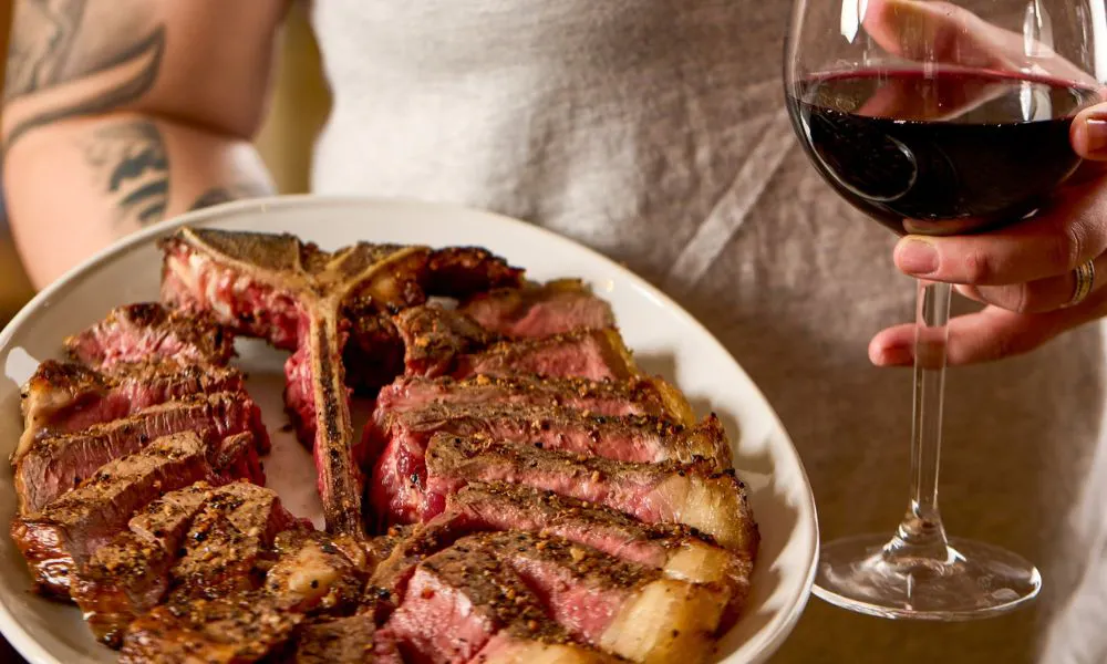 a steak and a glass of red wine being held