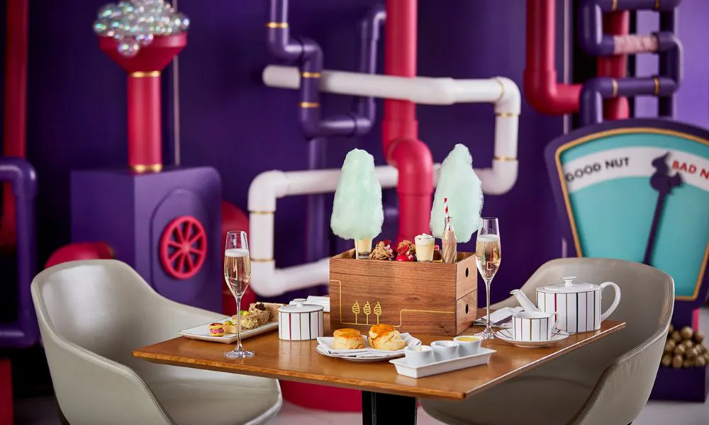 colourful backdrop with a table set with a box of cakes with chocolate milk and candy floss