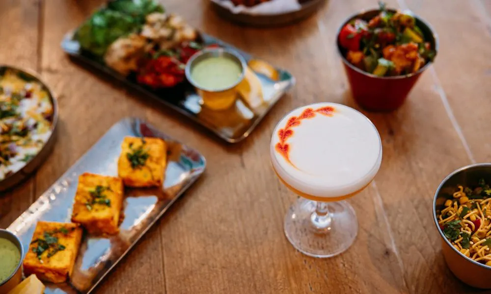 Foamed cocktail with plates of indian snacks