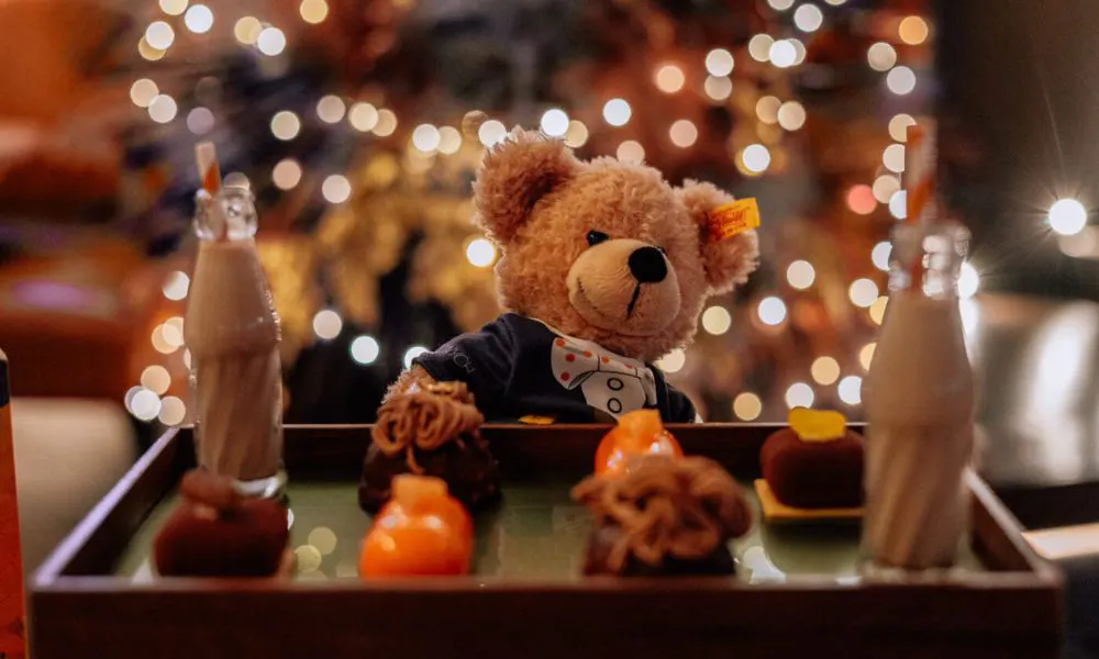 a teddy bear with a chocolate milkshake and a box of afternoon tea sweets
