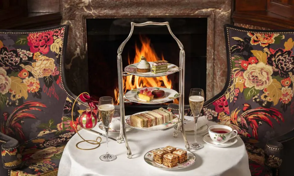 afternoon tea stand on a white-clothed table, with floral armchairs and a roaring fire