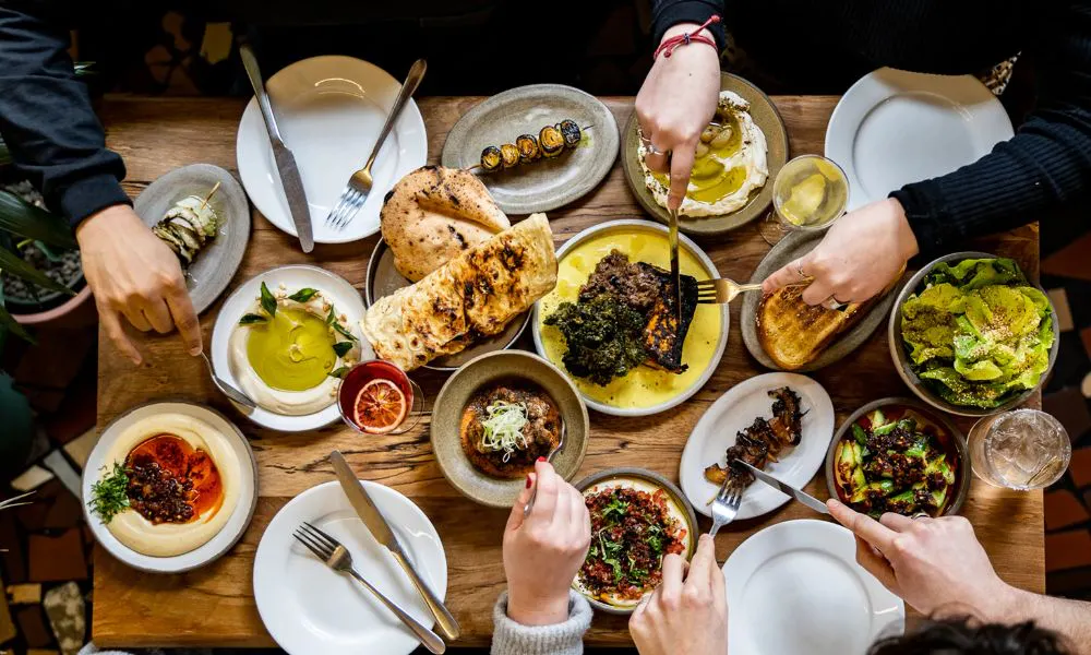 wood table with dip bowls, bread, and grilled veg