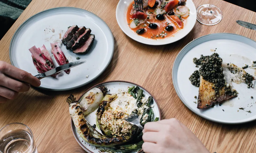 hands use cutlery to cut plates of meat and veg