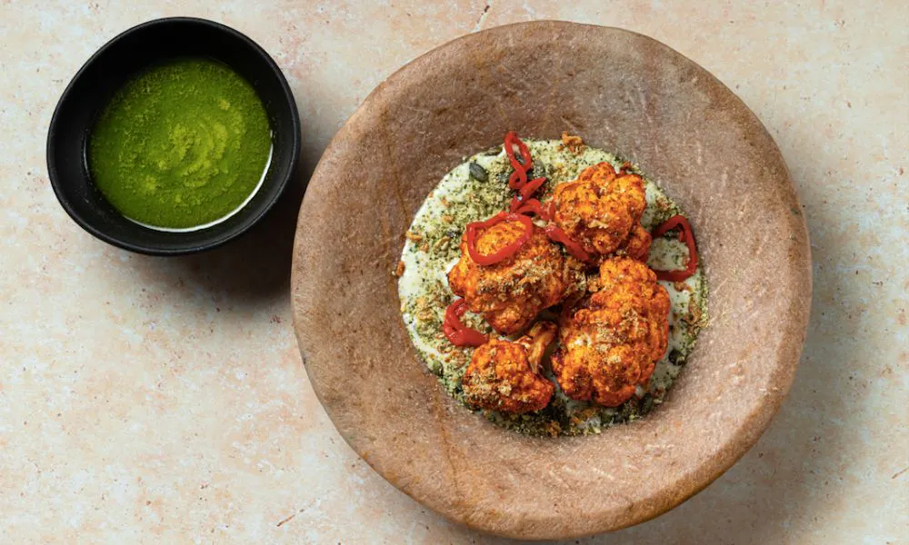 A bowl of fried cauliflower on a green sauce