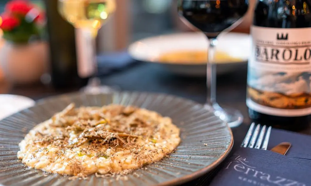 Black plate with brown risotto and bottle of barolo