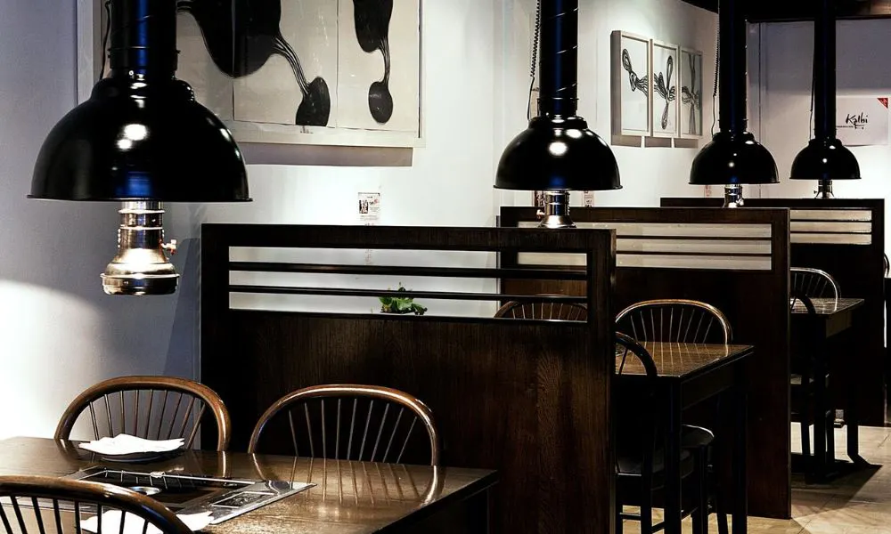 A dark dining room with booth seating and grills on each table