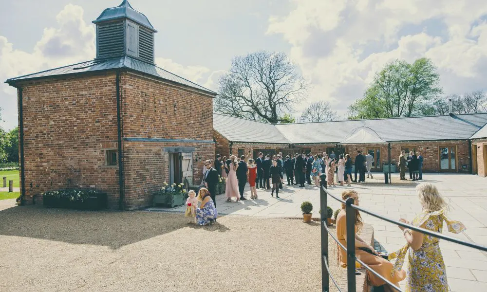 Guests mingle outside red brick wedding hall