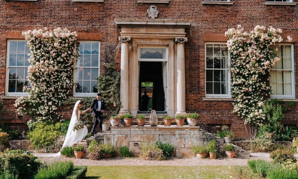 groom leads bride up steps to red brick manor