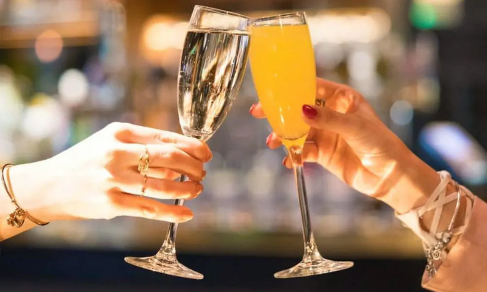 Two hands cheersing with a glass of Prosecco and a mimosa 