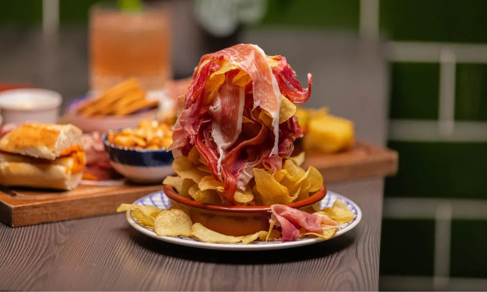 A selection of tapas plates and bocadillos with crisps and ham on a table