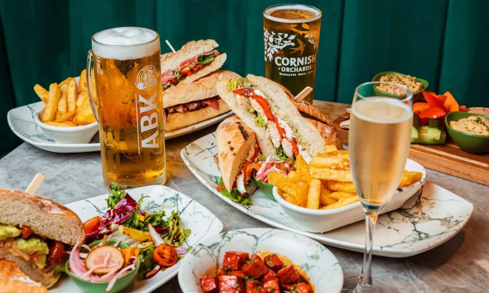 A table covered with plates of sandwiches and chips, served with beers and prosecco