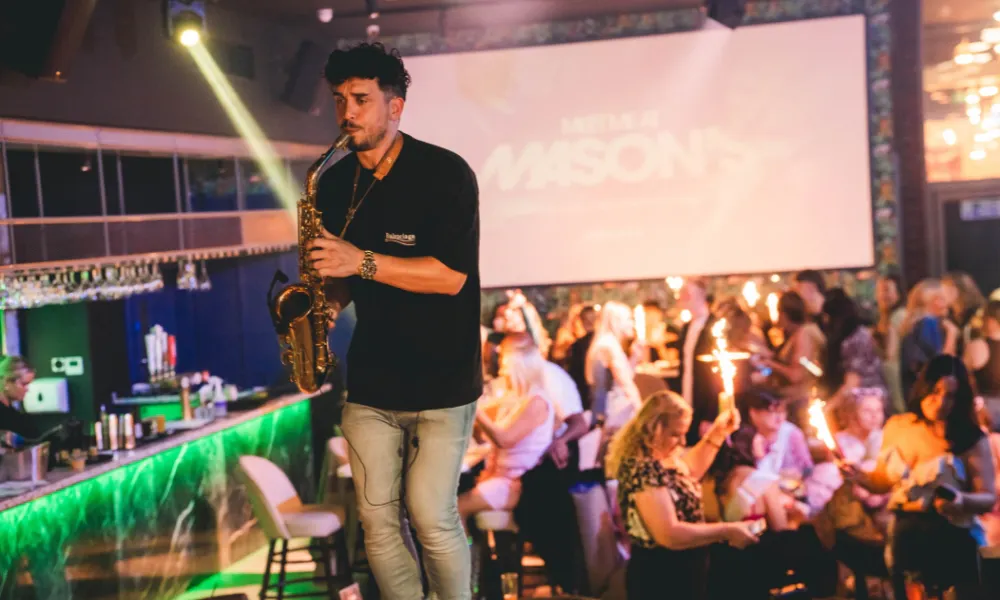 A man playing a saxophone on a table amongst crowds of people enjoying brunch