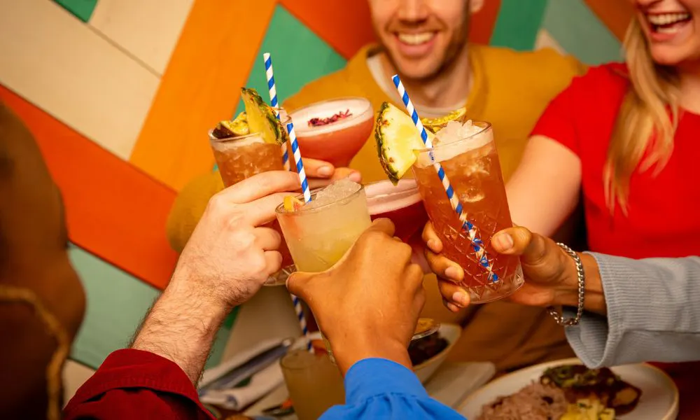 A group of people cheering with a mix of cocktails against a colourful background