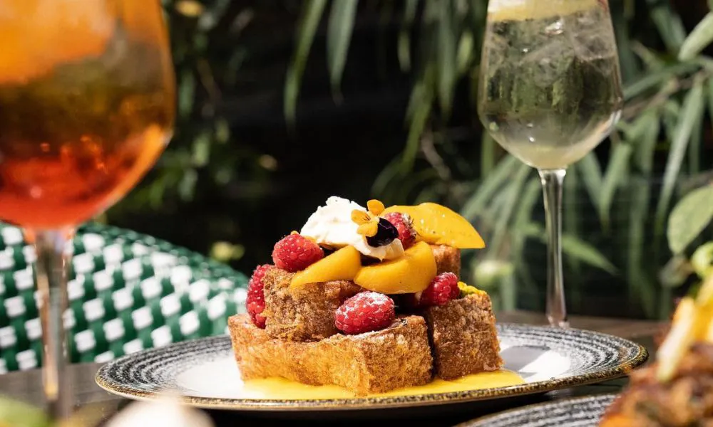 French toast with raspberries and peaches on a table, with a couple of cocktails